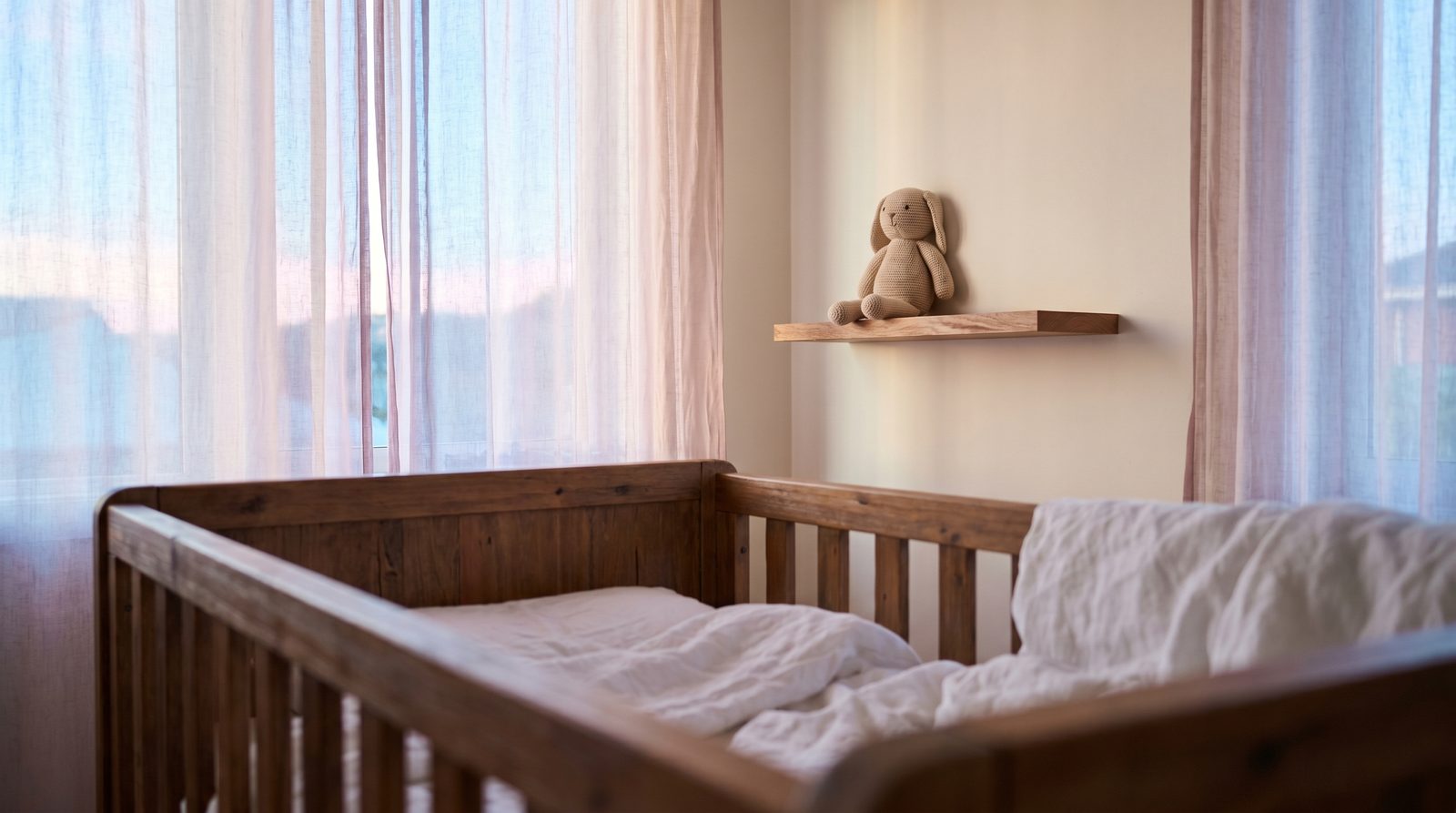 A soft nursery scene at dawn with a wooden crib and sheer curtains glowing with early morning light